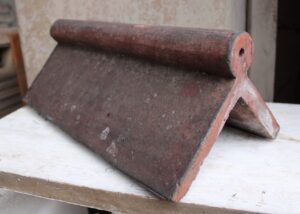 Reclaimed red fancy ridge tile with a roll top design, perfectly angled at 90 degrees, showcasing its rich colour and classic elegance, ideal for adding a historical touch to modern and traditional roofs alike.